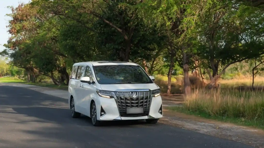 Toyota Alphard putih melaju di jalan pedesaan Bali yang rindang