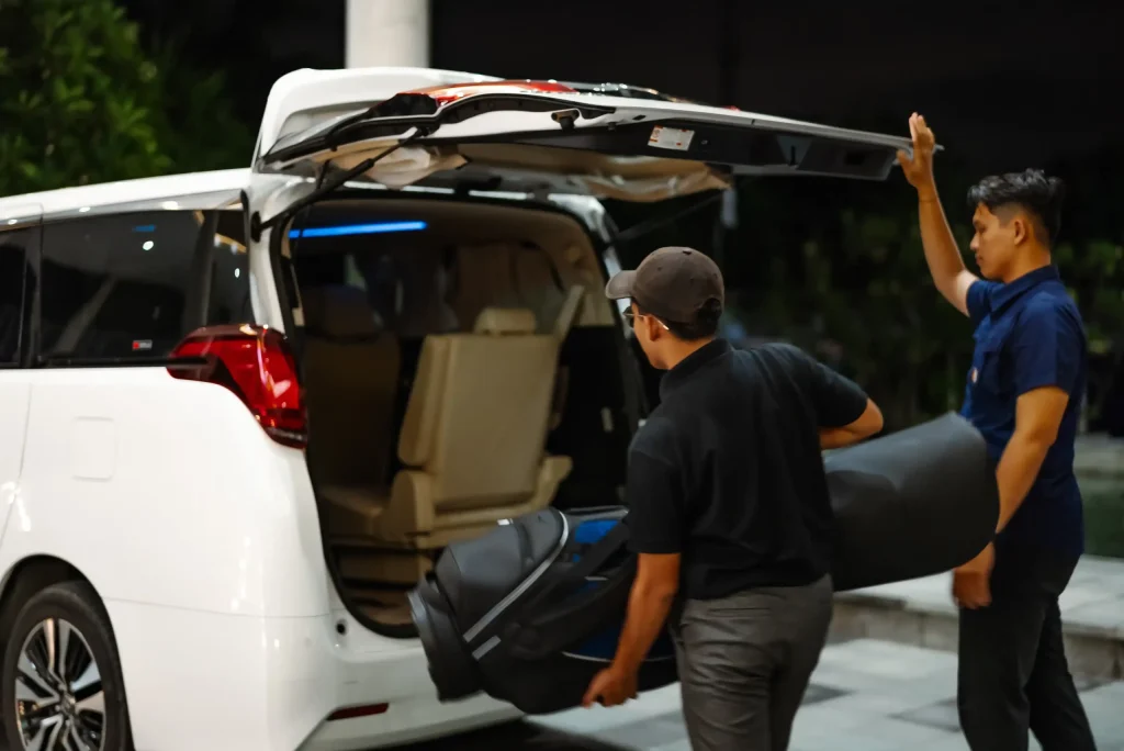 Petugas memuat tas ke bagasi Toyota Alphard putih